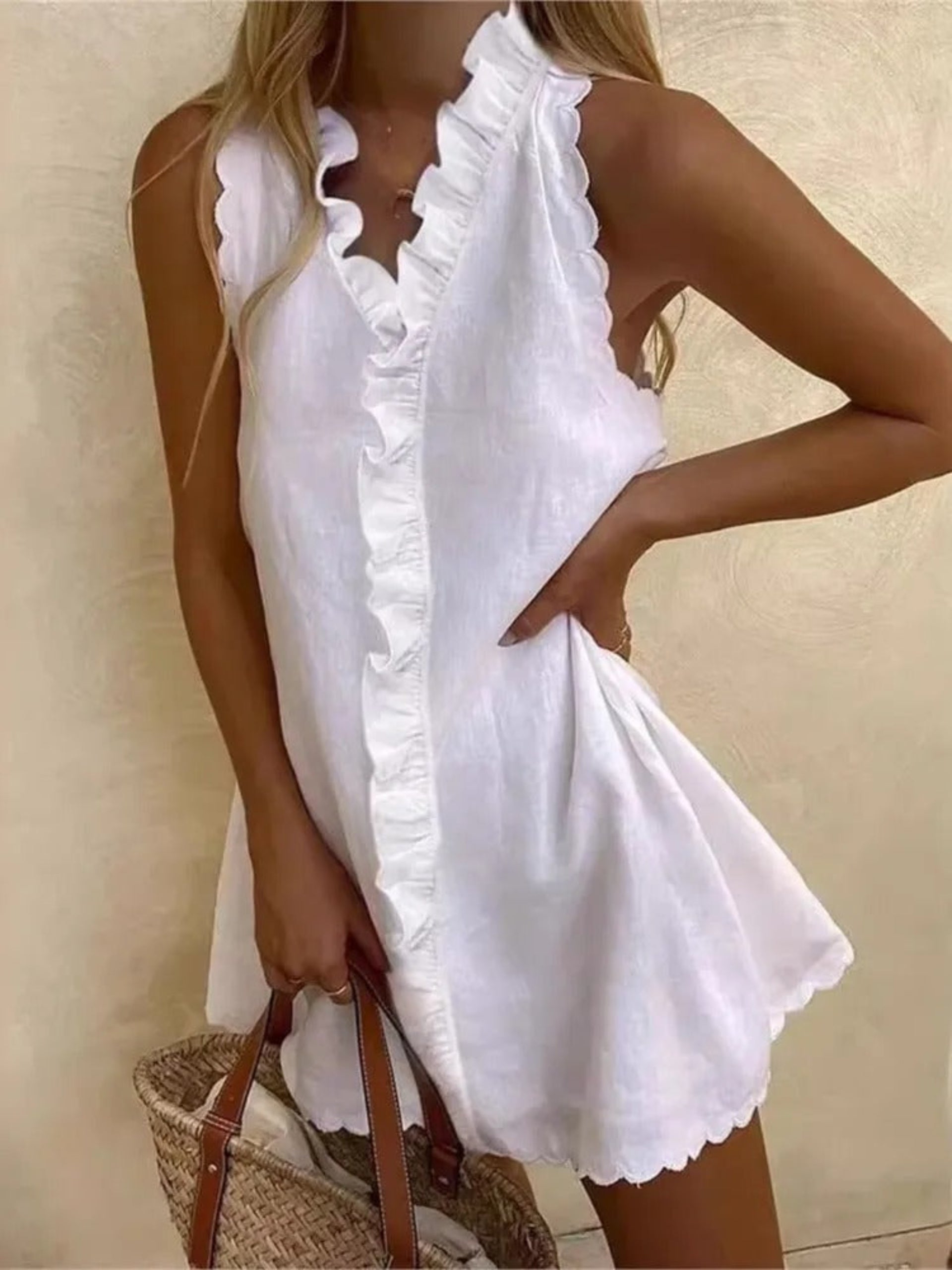 Woman wearing white sleeveless ruffled linen mini dress with woven straw beach bag