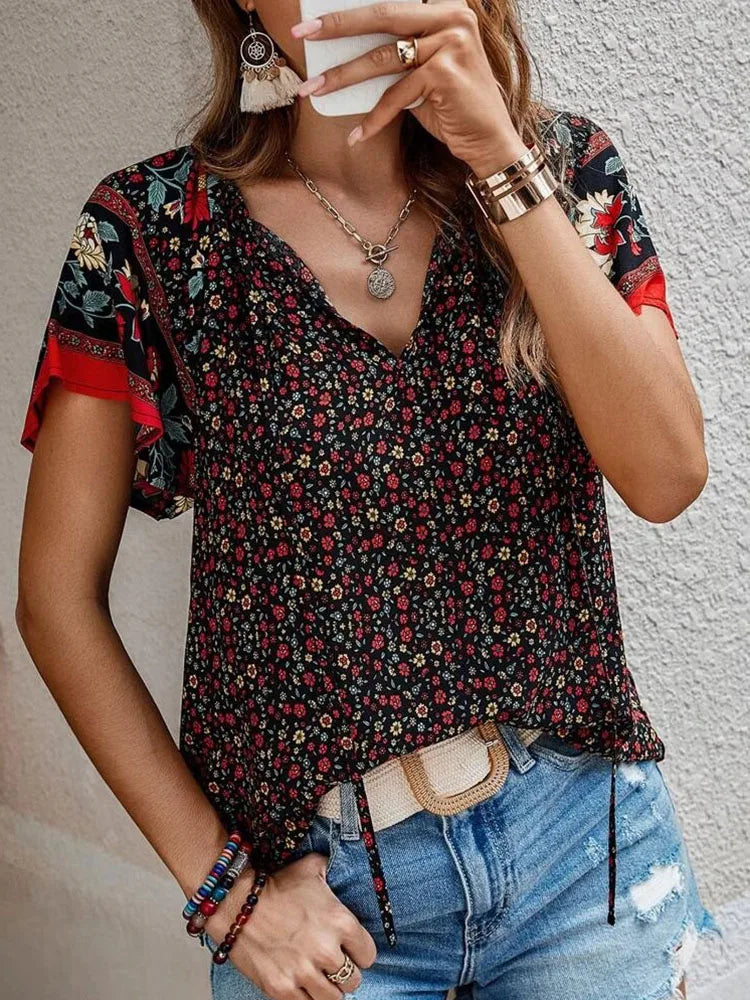 Woman wearing black boho floral print blouse with red accents, V-neck design, styled with denim jeans and gold jewelry