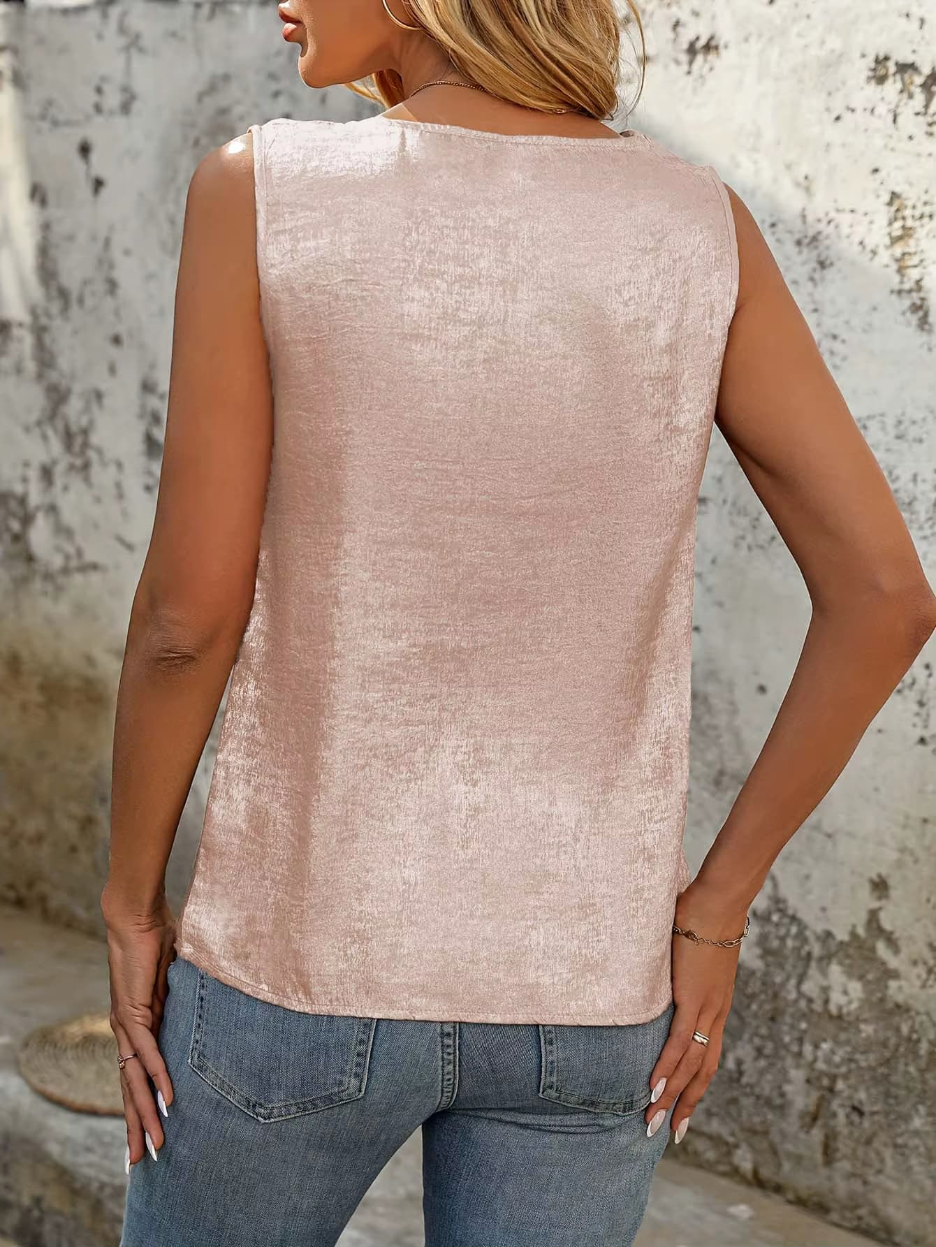 Woman wearing sleeveless satin top with asymmetrical neckline and button detail in pink
