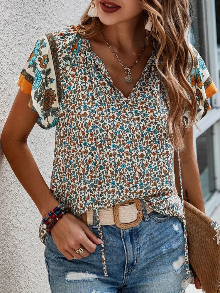 Woman wearing cream boho floral print blouse with turquoise and orange floral sleeves, V-neck design, styled with distressed denim jeans and gold necklace