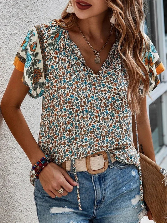 Woman wearing cream boho floral print blouse with turquoise and orange floral sleeves, V-neck design, styled with distressed denim jeans and gold necklace