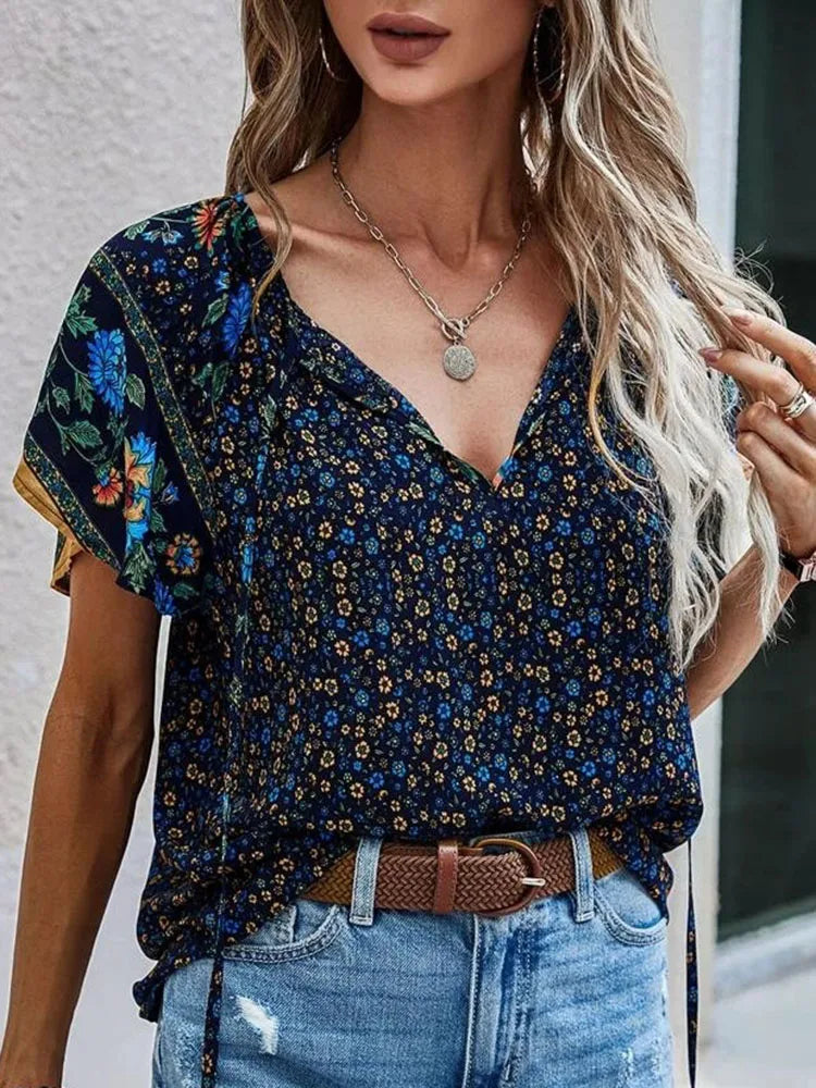 Woman wearing navy blue boho floral print blouse with colorful floral sleeves and V-neck, styled with distressed denim jeans and braided belt