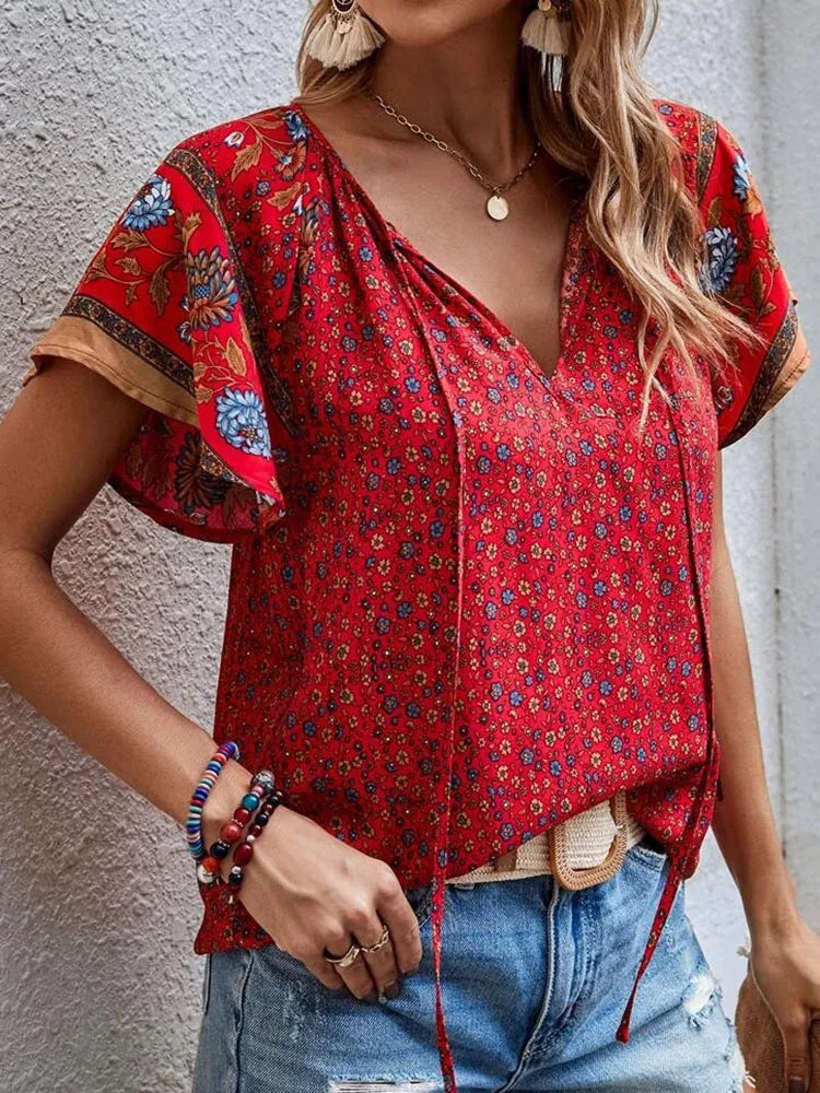 Woman wearing red boho floral print blouse with V-neck and decorative sleeves, styled with denim jeans and gold pendant necklace