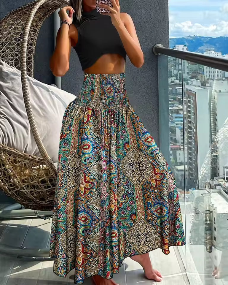 Woman wearing black crop top and a colorful paisley print maxi skirt in teal, red, and gold with smocked waist