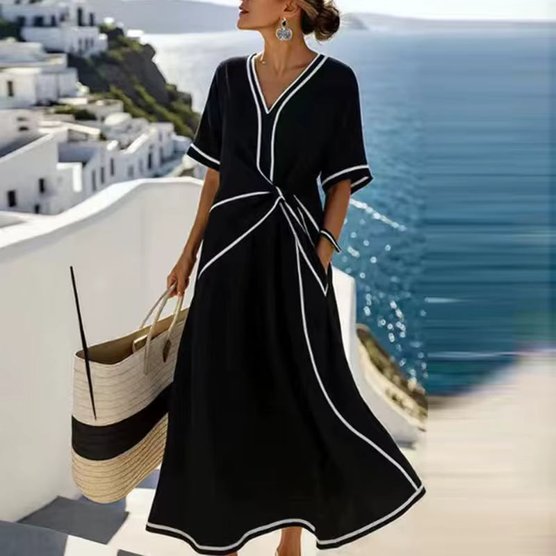 Woman wearing black, white-trimmed A-line midi dress with twist-front, V-neck and short sleeves